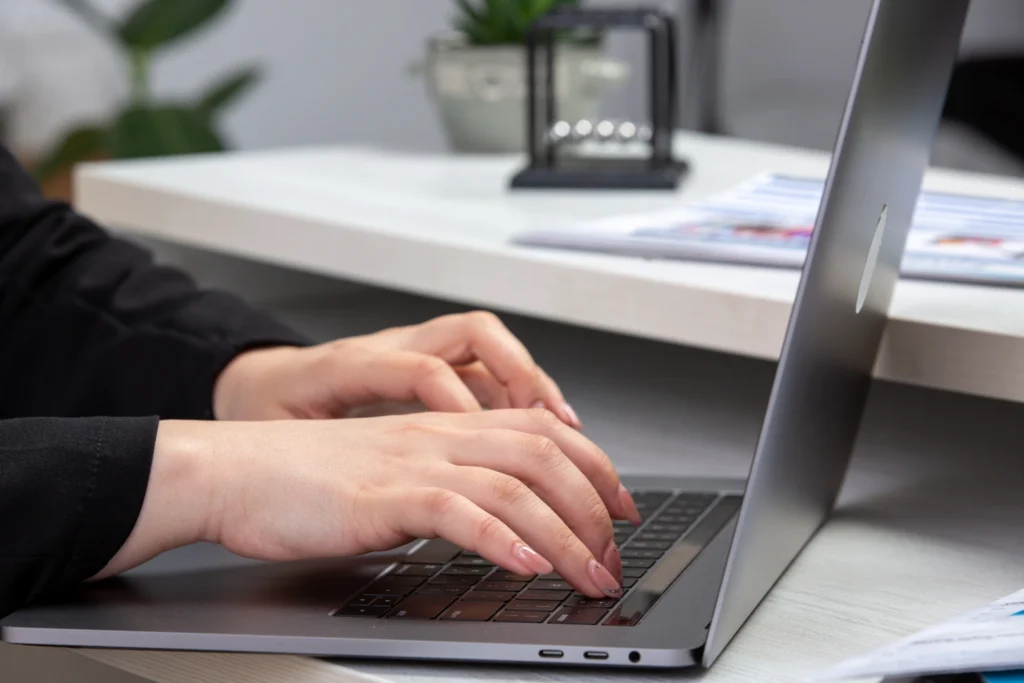 Female hands typing on a slim laptop at a minimalist desk.